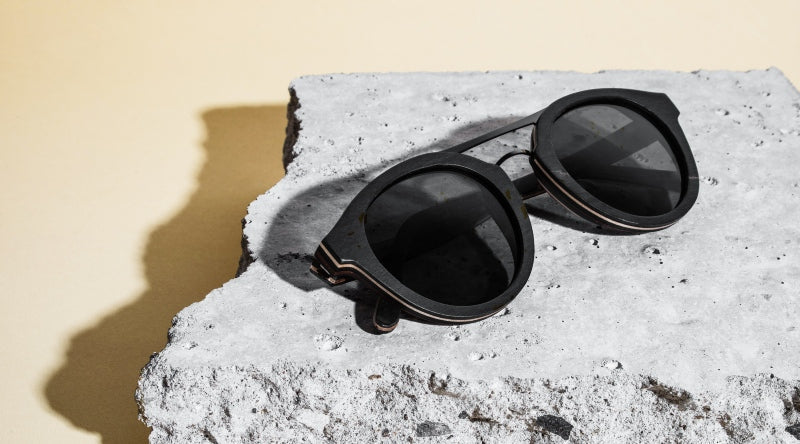 flatlay of Ash sunglasses on a grey rock with light pink background