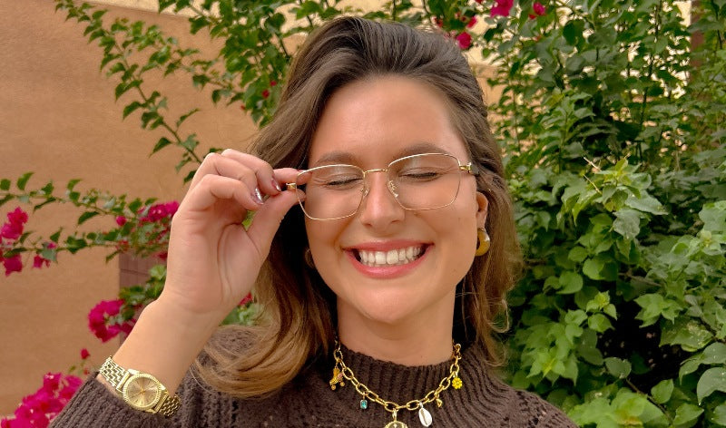 woman smiling and wearing fair gold metal eco friendly glasses with trees in background