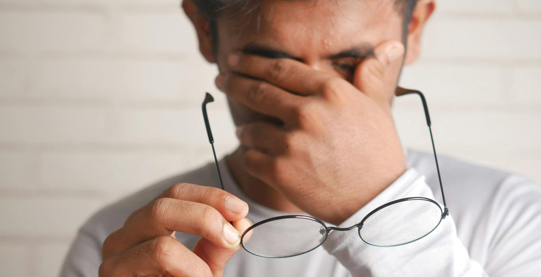 man experiencing eye fatigue, rubbing his eyes while holding his glasses