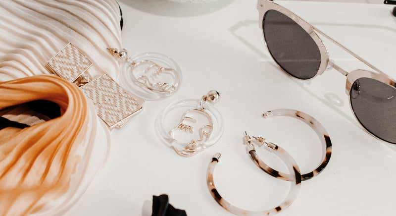 trending accessories including sunglasses and artistic earrings on white table
