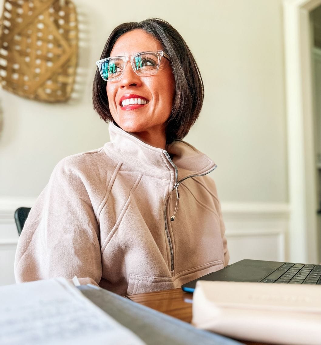 Woman wearing anti fatigue glasses sitting on a desk with a laptop and books.