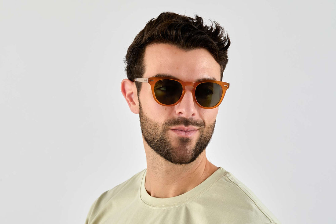 Homme portant des lunettes de soleil de forme ronde et carrée orange avec des verres verts polarisés au coucher du soleil